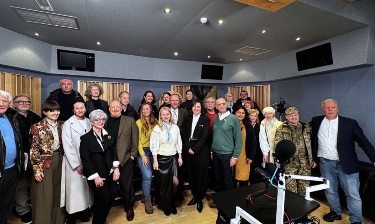 A large group of guests and speakers standing together after a roundtable in a studio